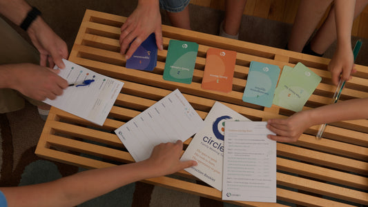 Family of five gathered around a modern coffee table with the Circle In family meeting toolkit pieces spread on top, family reaching for different pieces