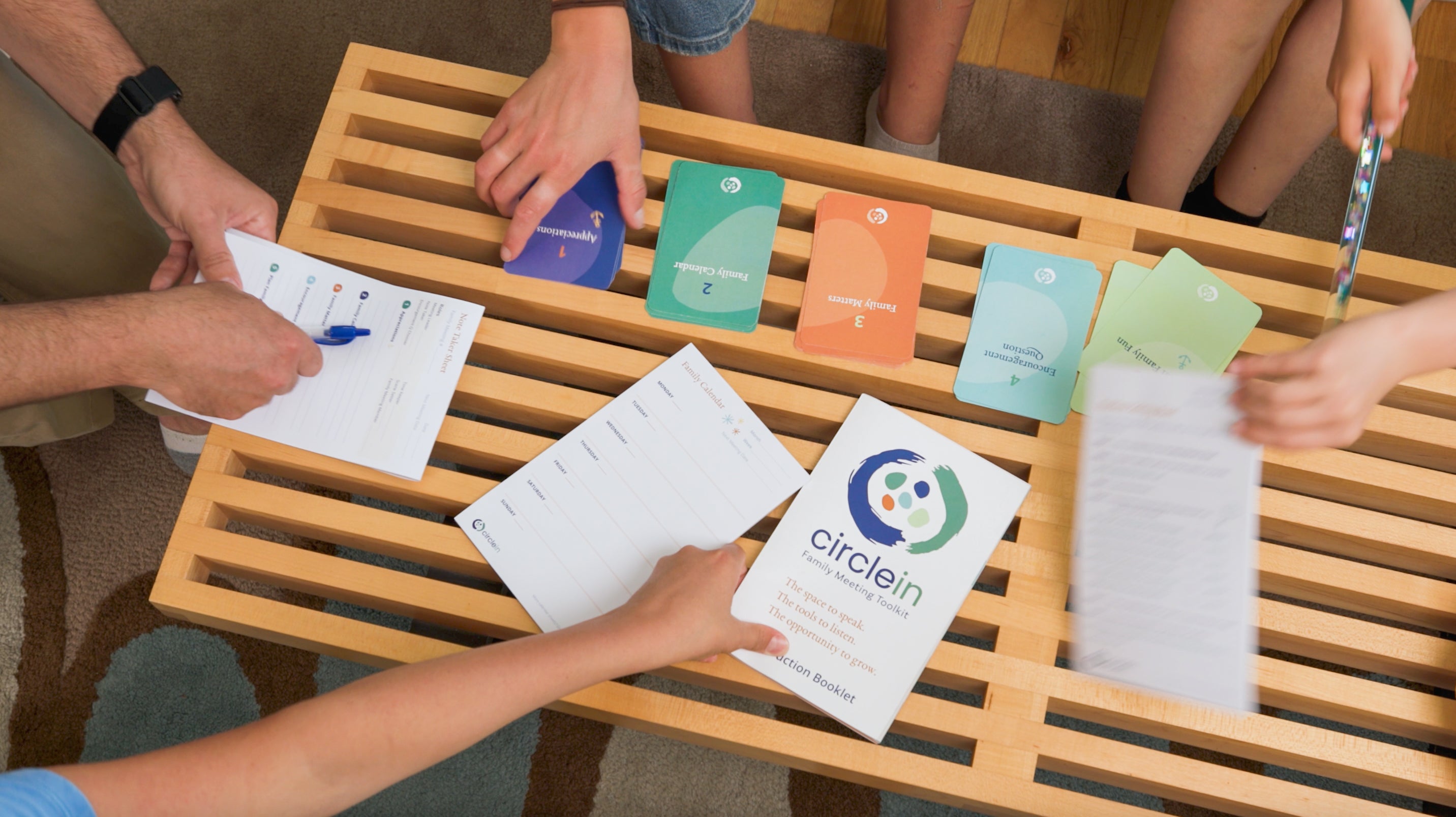 Family of five gathered around a modern coffee table with the Circle In family meeting toolkit pieces spread on top, family reaching for different pieces