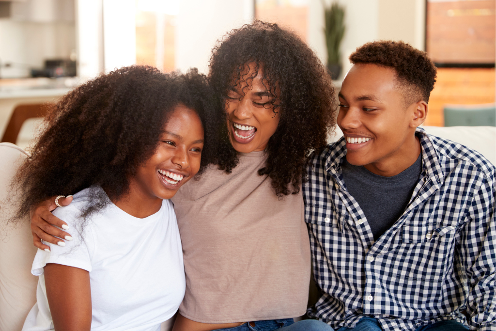 Family of three sitting together on a couch, smiling and laughing.