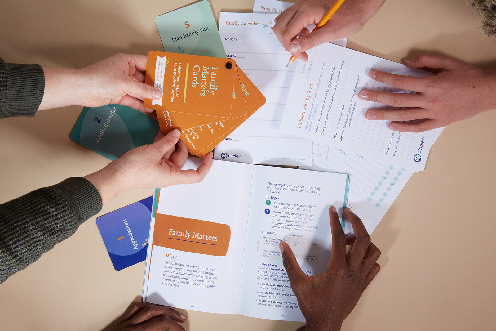 Hands interacting with the items in Family Meeting Kit, including cards, instructional booklet and notepad.