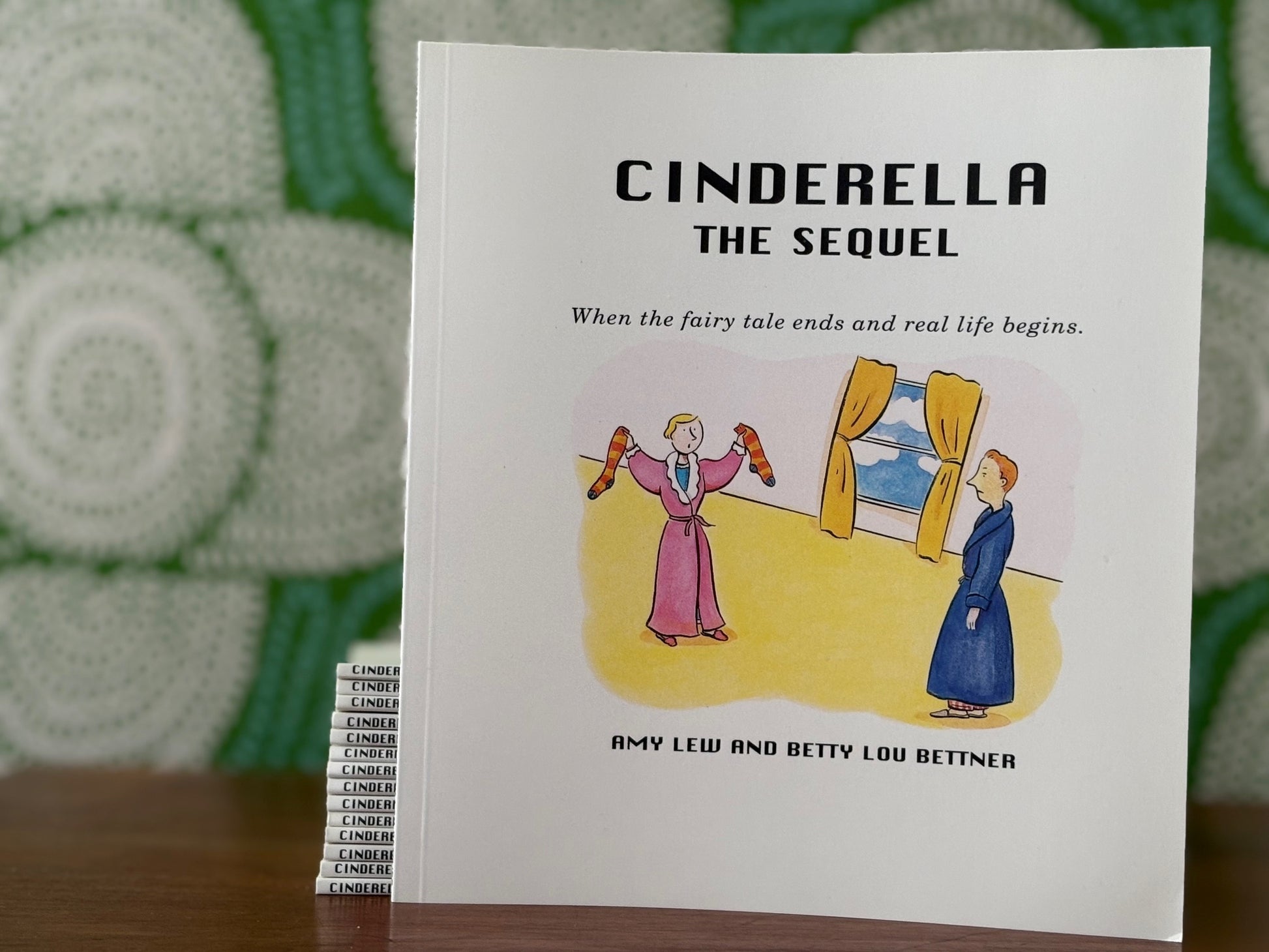 Stack of books titled 'Cinderella The Sequel: When the Fairy Tale Ends and Real Life Begins' with illustration on the cover in front of a green patterned background