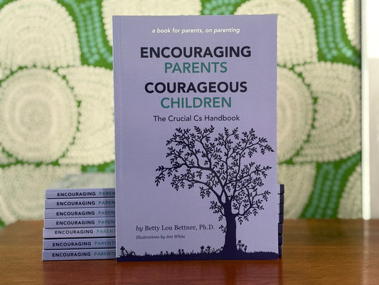 Stack of books titled 'Encouraging Parents, Courageous Children' on a wooden surface with a textured green background.