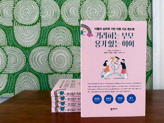 Pink book with Korean text propped up against a green patterned background. Book cover has family with ball.
