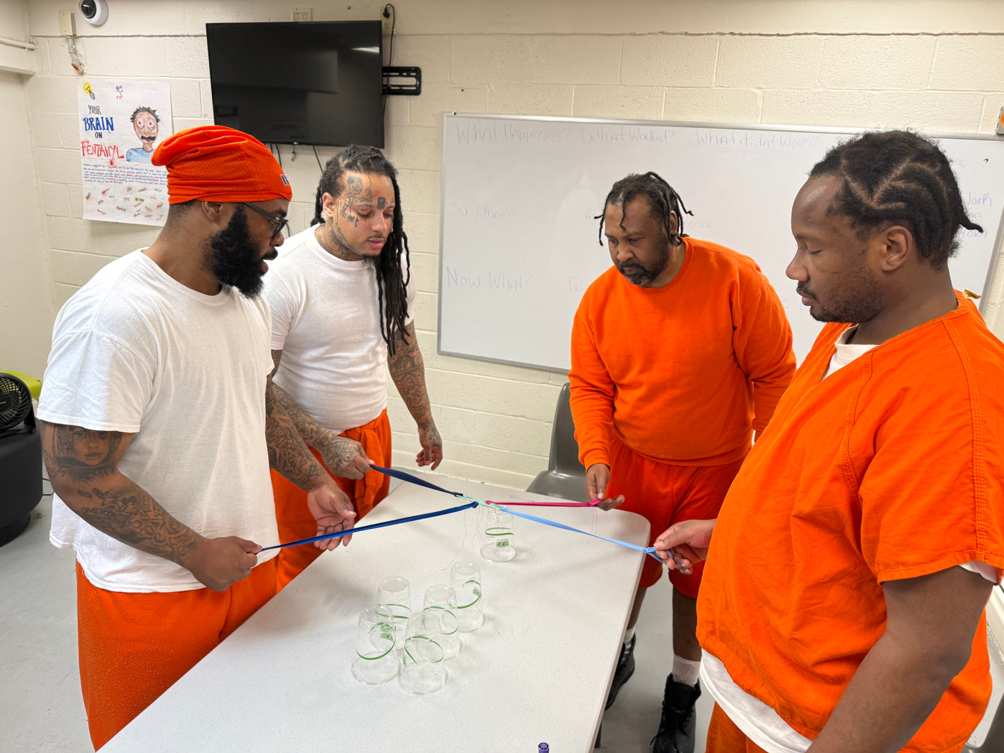 Four men in orange uniforms playing cooperative cup stacking game.