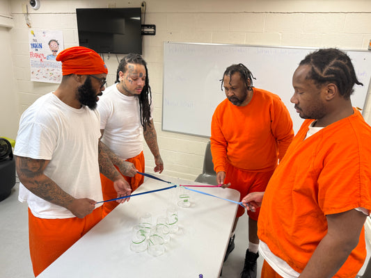 Four men in orange uniforms playing cooperative cup stacking game.